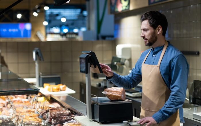 Butcher working in grocery store using digital scales to weigh deli meats