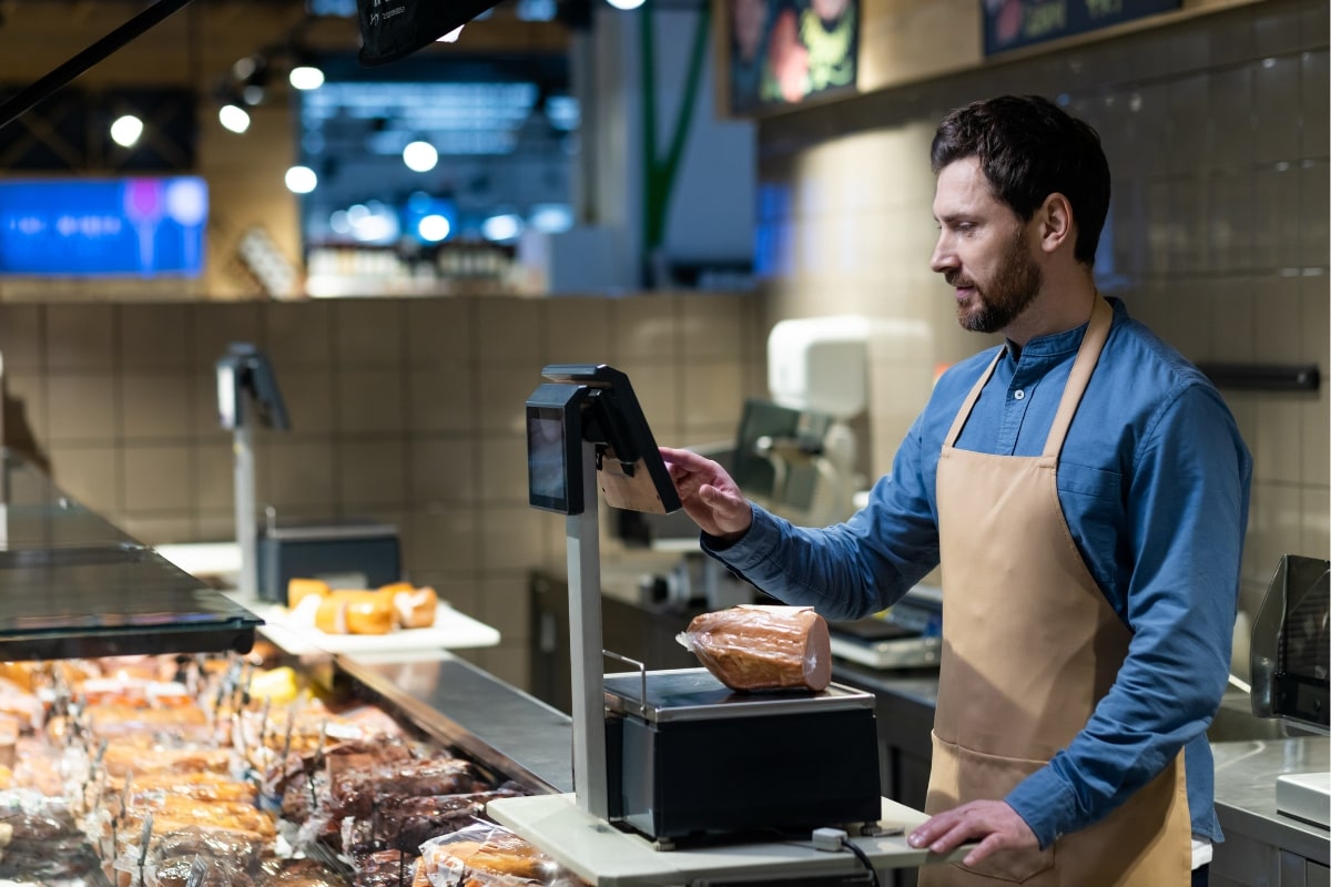 Butcher working in grocery store using digital scales to weigh deli meats